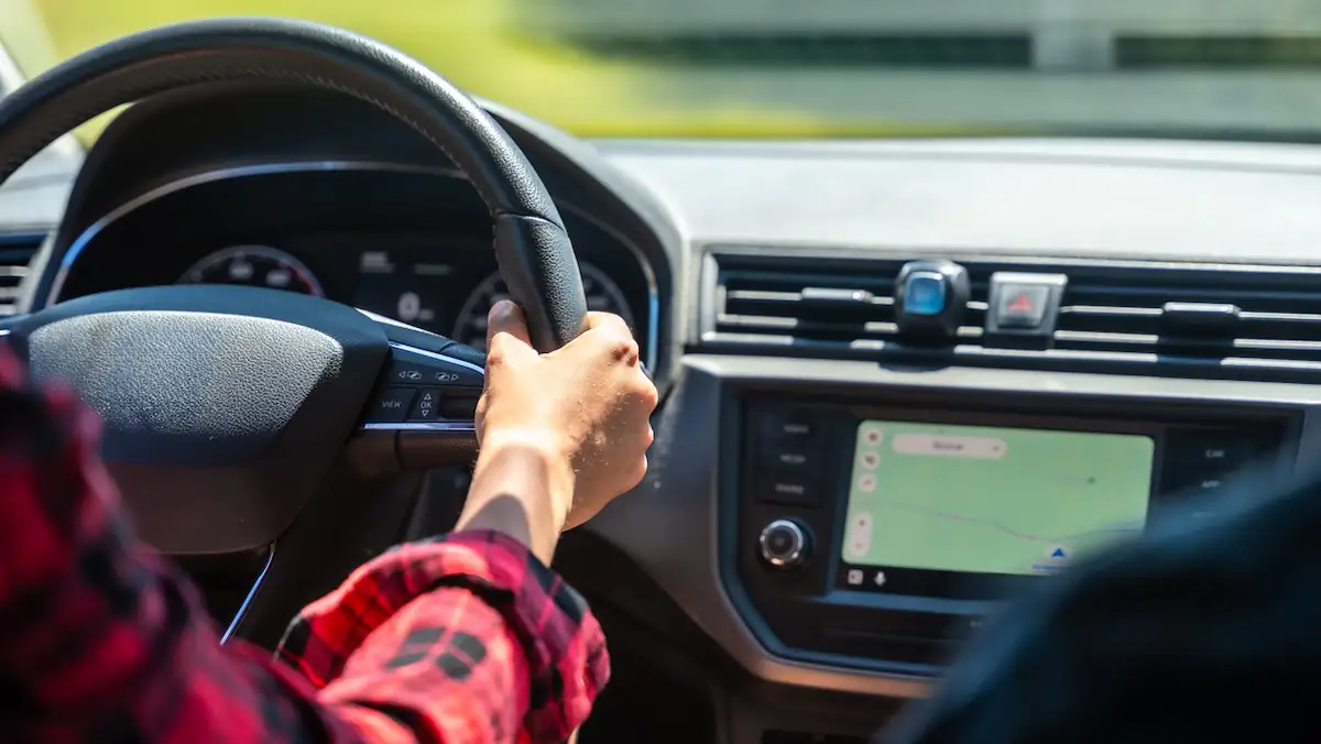 Angeschnittener Arm einer Autofahrerin, die beide Hände am Lenkrad hat