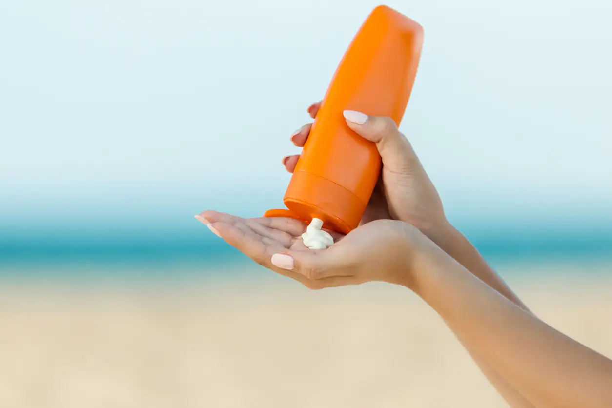Hautkrebsrisiko durch Sonnenbaden: Frauenhand hält Tube mit Sonnencreme und drückt etwas davon auf die Hand