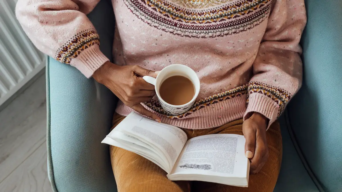 Lesen: Frau sitzt mit einem buch auf dem Schoß und einer Tasse Kaffee