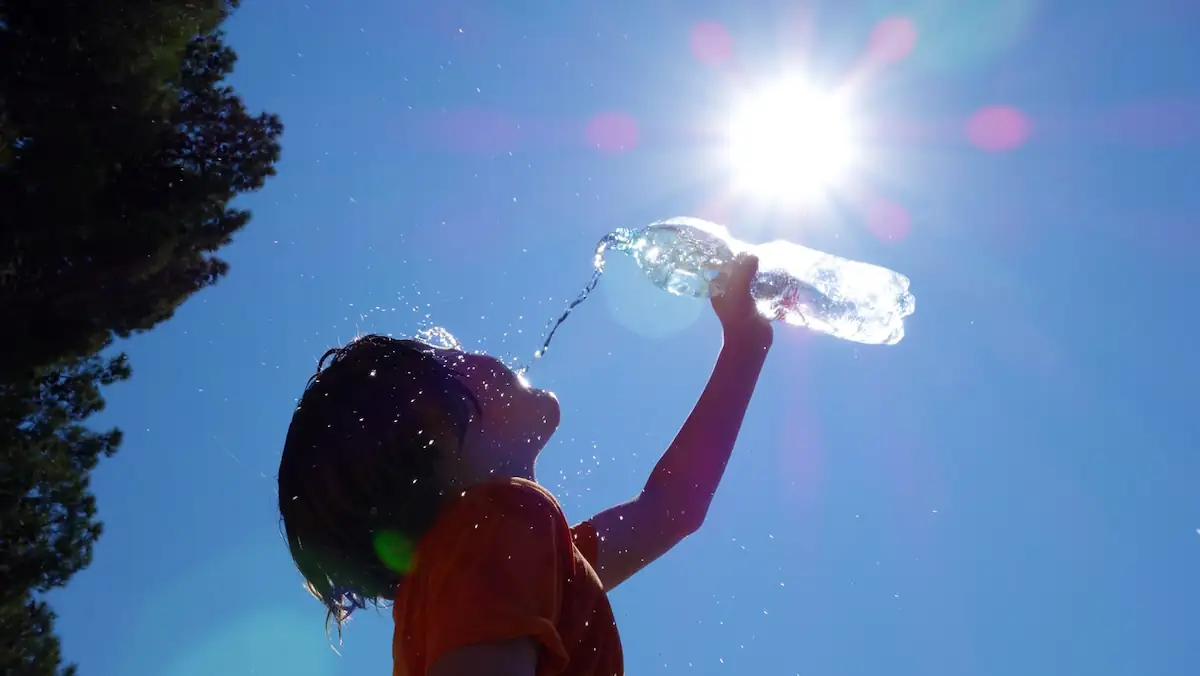 Schwitzen: Kind kühlt sich bei Sonnenschein mit Wasser aus einer Flasche