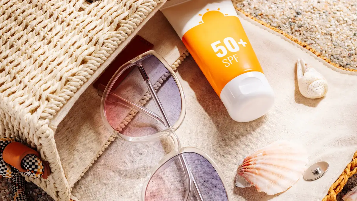 Sonnencreme mit Sonnenbrille und Muscheln auf einer Strandtasche