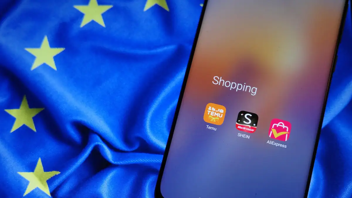 App Icons der Anbieter Temu, Shein und ALi Express auf einem Smartphone, das auf einer EU-Flagge liegt