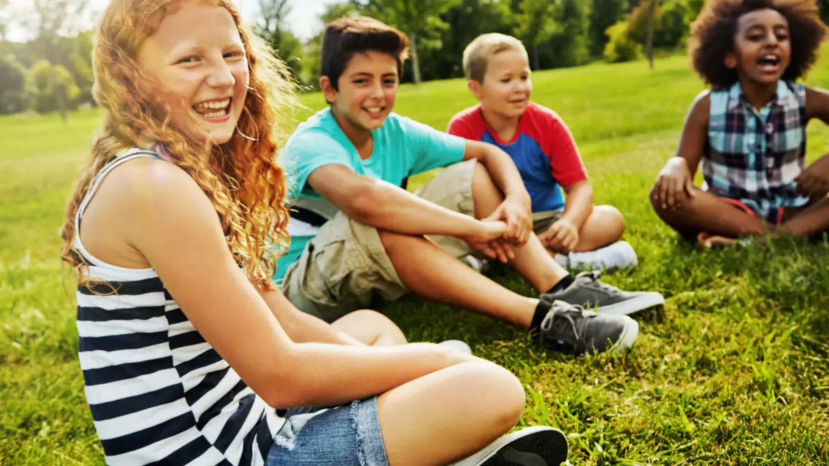 Sommerferien Symbolbild: Kinder sitzen auf einer Wiese und lachen