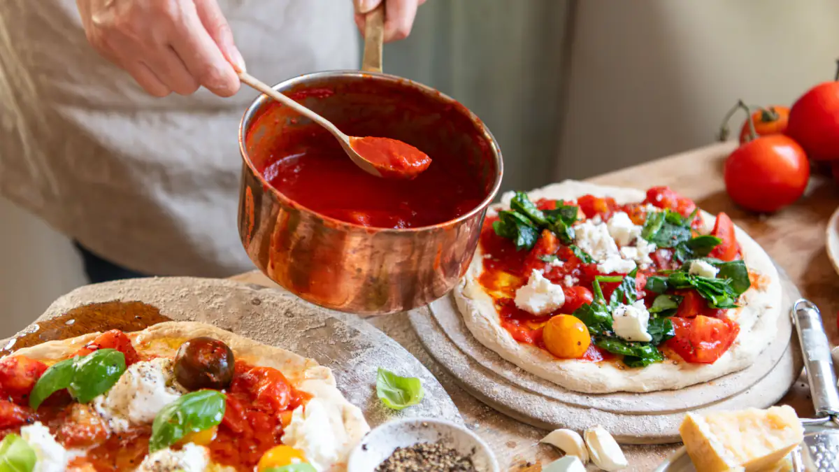 Frau kocht selbstgemachte Pizza mit Tomatensoße