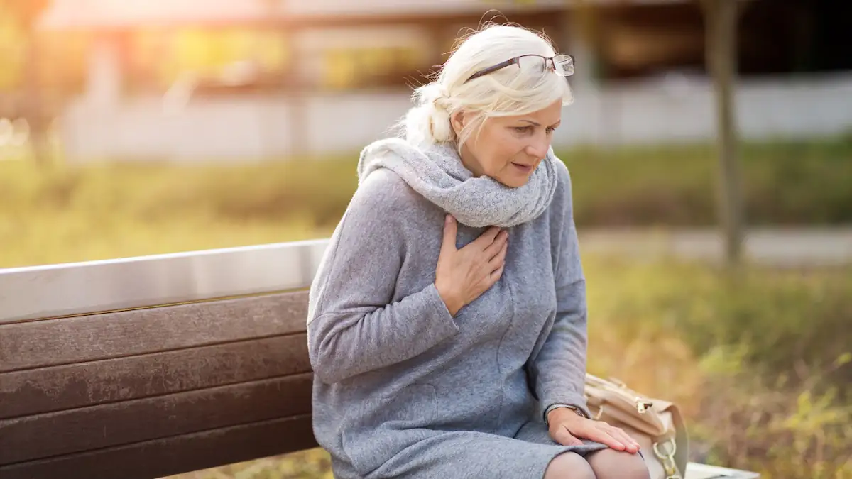 Happy Heart Syndrom: Ältere Frau sitzt auf einer Parkbank und greift sich an die Brust