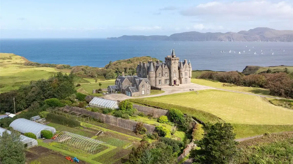 Glengorm Castle von oben aus der Ferne, daneben sind einige landwirtschaftliche Gebäude zu sehen (Schloss steht zum Verkauf