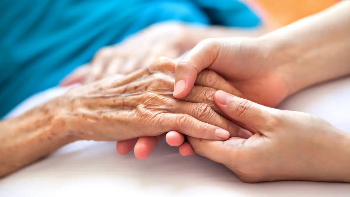 Alzheimer-Symbolbild: Nahaufnahme von zwei Personen, die sich an den Händen fassen, wobei die eine deutlich älter ist als die andere