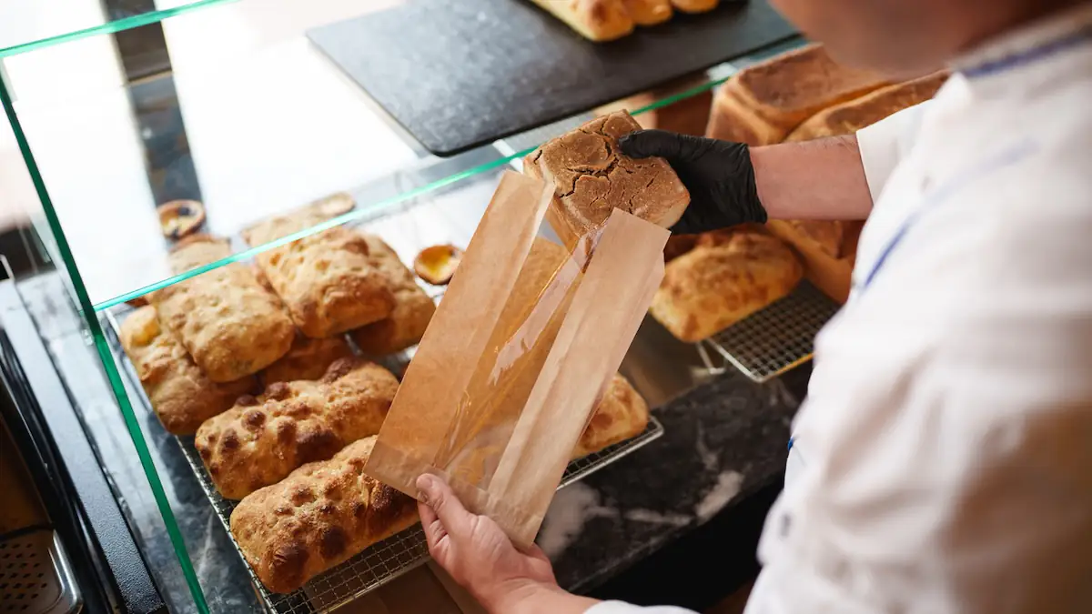 Neue EU-Richtlinien für Lebensmittelverpackungen Symbolbild: Bäcker packt Brötchen in eine Tüte