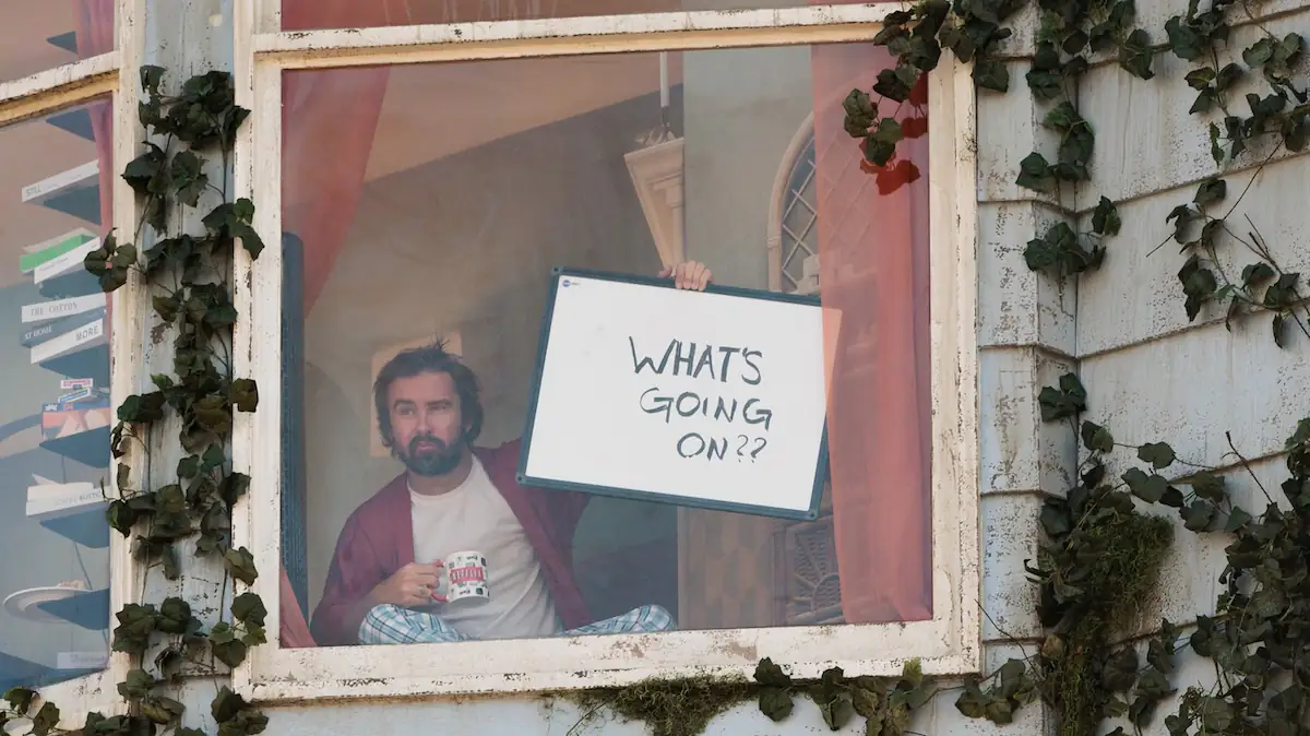 Szene aus dem Netflix-Film „The Last House“, in der ein Mann ein Schild mit der Aufschrift „What's going on?“ ins Fenster hält
