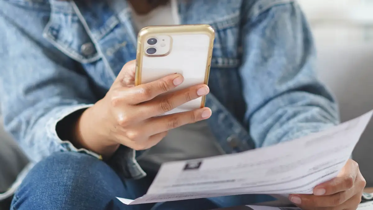Symbolbild Grundsteuer: Person hält Smartphone und Unterlagen in der Hand