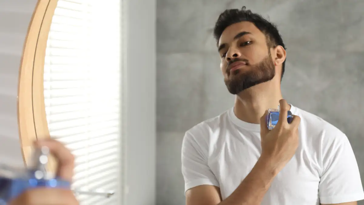 Ein Mann benutzt Parfum vorm Spiegel