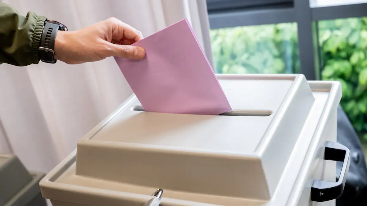 Kanzlertausch Debatte Symbolbild: Rosafarbener Stimmzettel wird in eine Wahlurne gesteckt