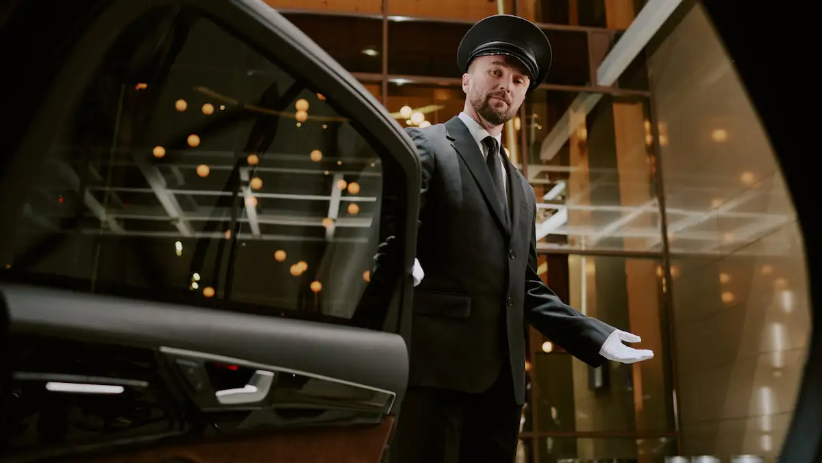 Luxusurlaub Symbolbild: Fahrer in Uniform öffnet die Tür eines luxuriösen Autos