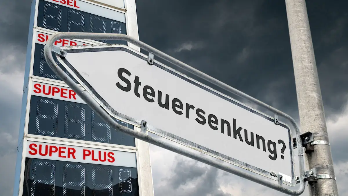 Schild zeigt Schriftzug „Steuersenkung“ im Hintergrund eine Preissäule für Sprit