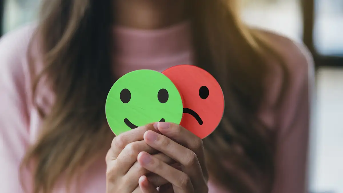 Ambivertierter Persönlichkeitstyp Symbolbild: Frau hält einen grünen lachenden und einen roten traurigen Smiley in der Hand