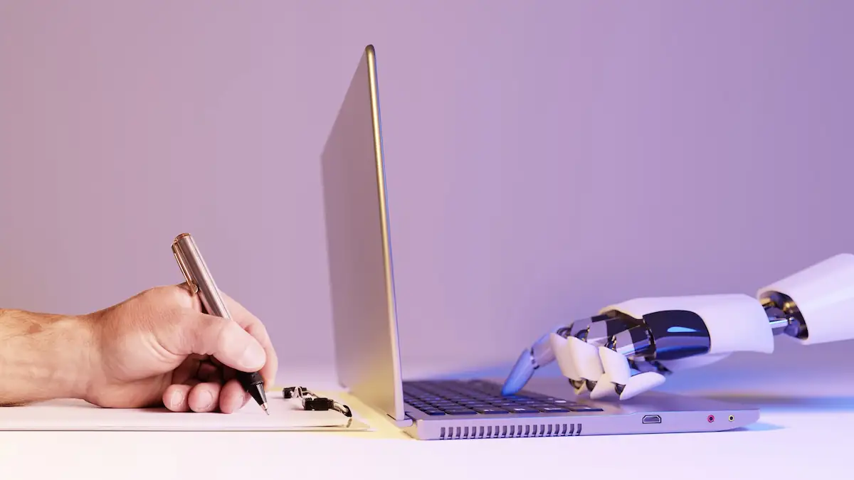 Bill Gates über KI Symbolbild: Links hält einen Mensch Stift und Papier, rechts schreibt eine Roboterhand auf einem Laptop